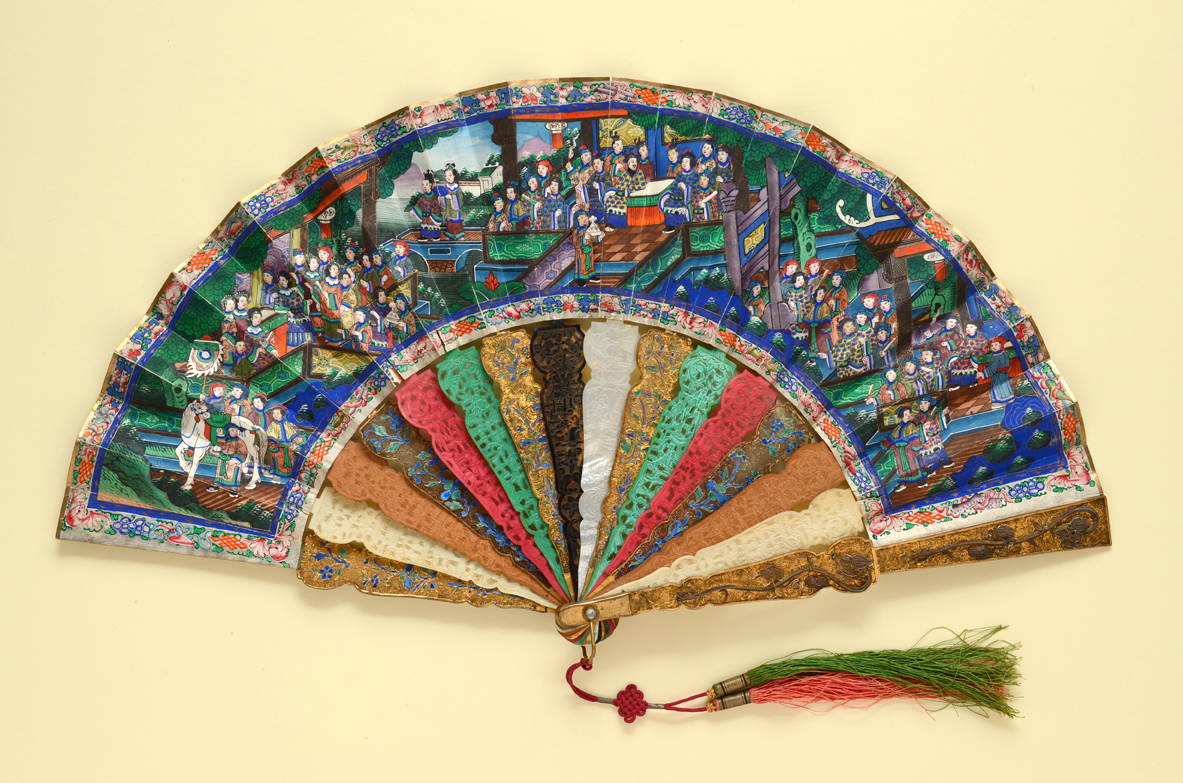 . ‘Applied Faces’ folding fan with lavish sticks of alternating materials. The double paper leaf is painted similarly on both sides with bustling scenes populated by Chinese officials and other figures with ivory faces and robes fashioned from fragments of silk.  Chinese (for export), ca.1880s The Fan Museum, LDFAN1990.1.1