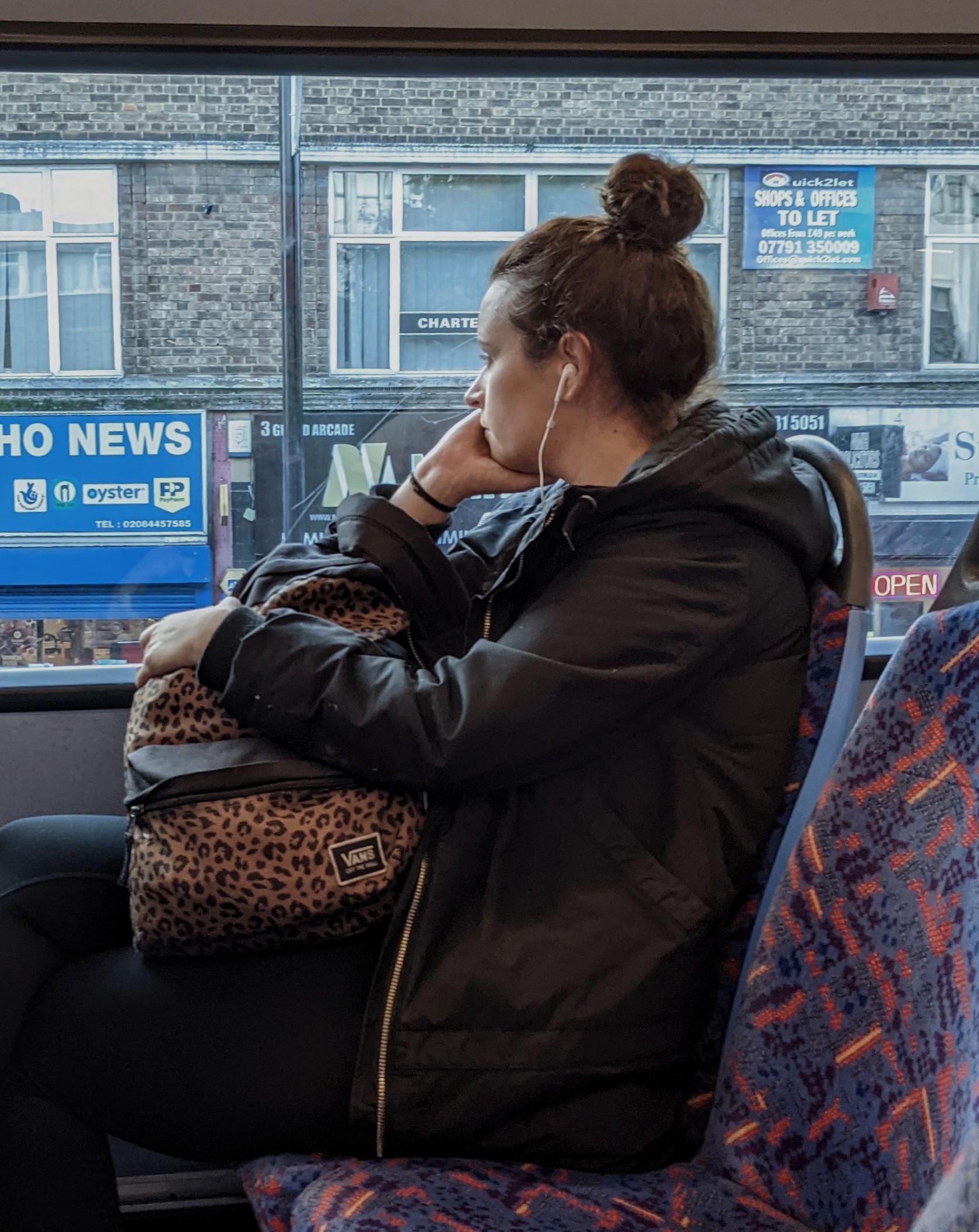 A photographic image of a woman looking out the window of a bus, with her face resting on her palm